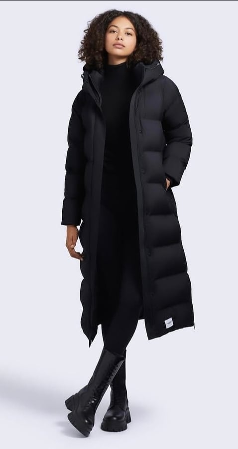 Woman wearing a long black puffer coat over a black turtleneck, paired with black boots