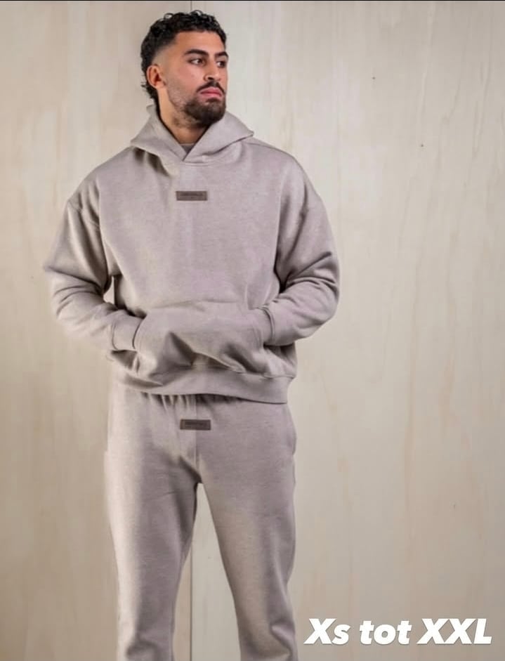 Man wearing light gray hoodie and matching sweatpants, standing against white background
