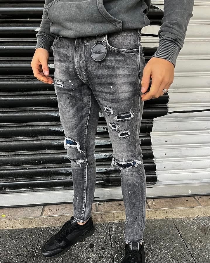 Person wearing distressed gray jeans with ripped knee details and chain wallet