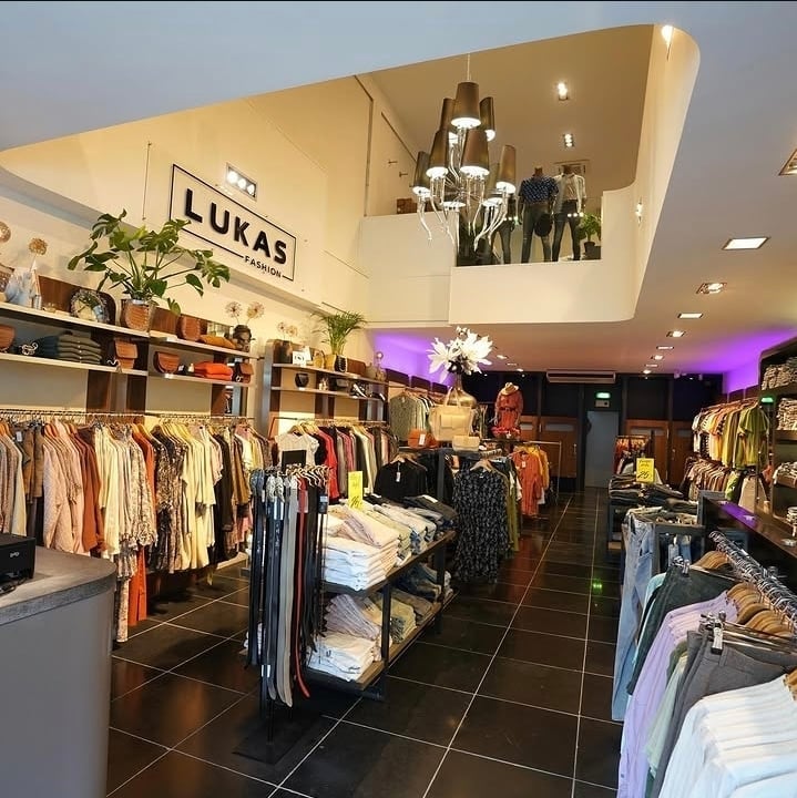 Interior of Lukas clothing retail store with clothing racks and modern purple-accented ceiling lighting