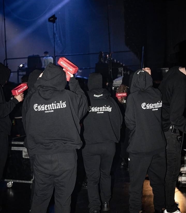 Group of people wearing black Essentials hoodies standing backstage under blue lighting
